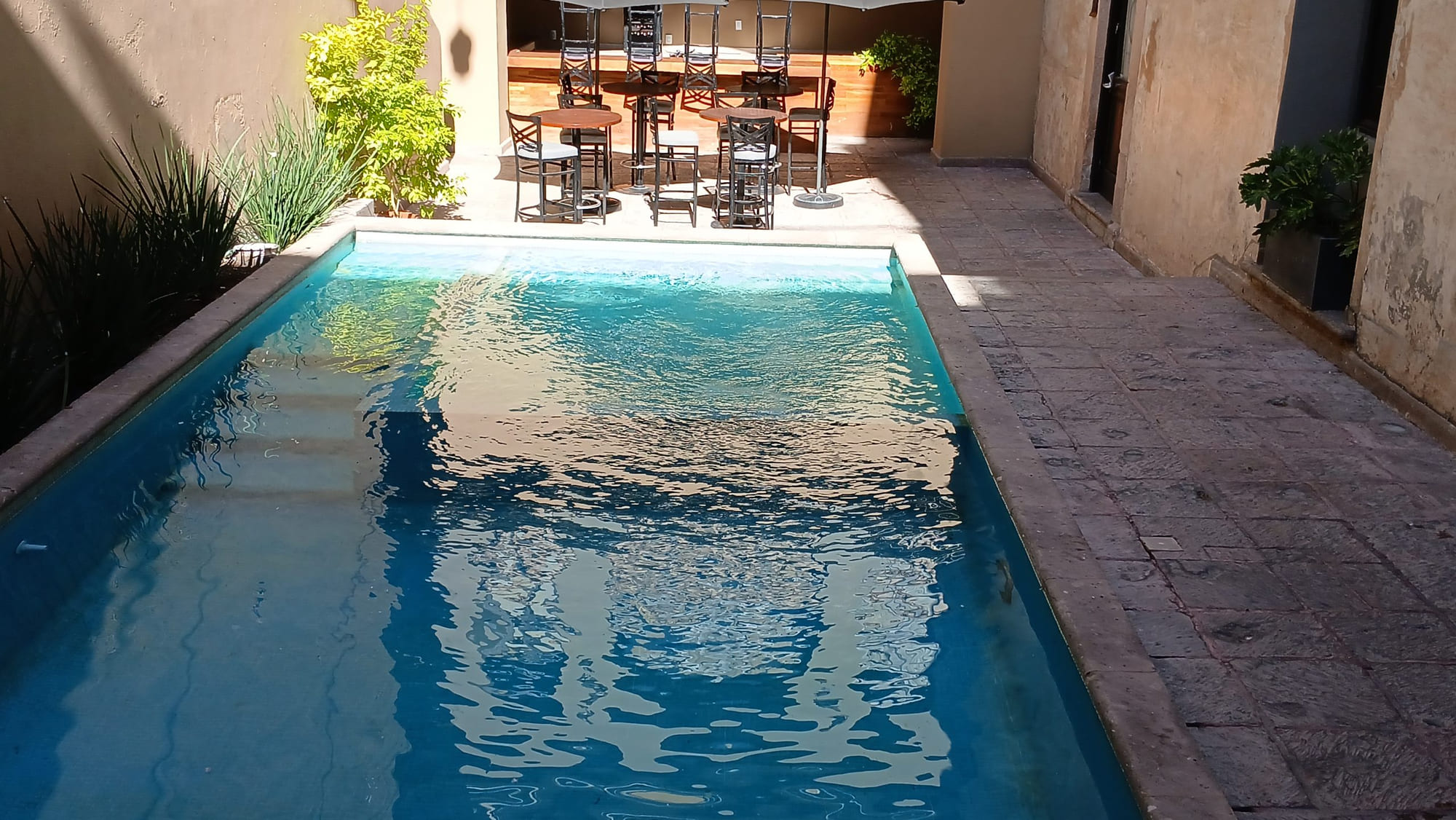 La alberca del hotel de día con la terraza de mesas en el nivel superior
