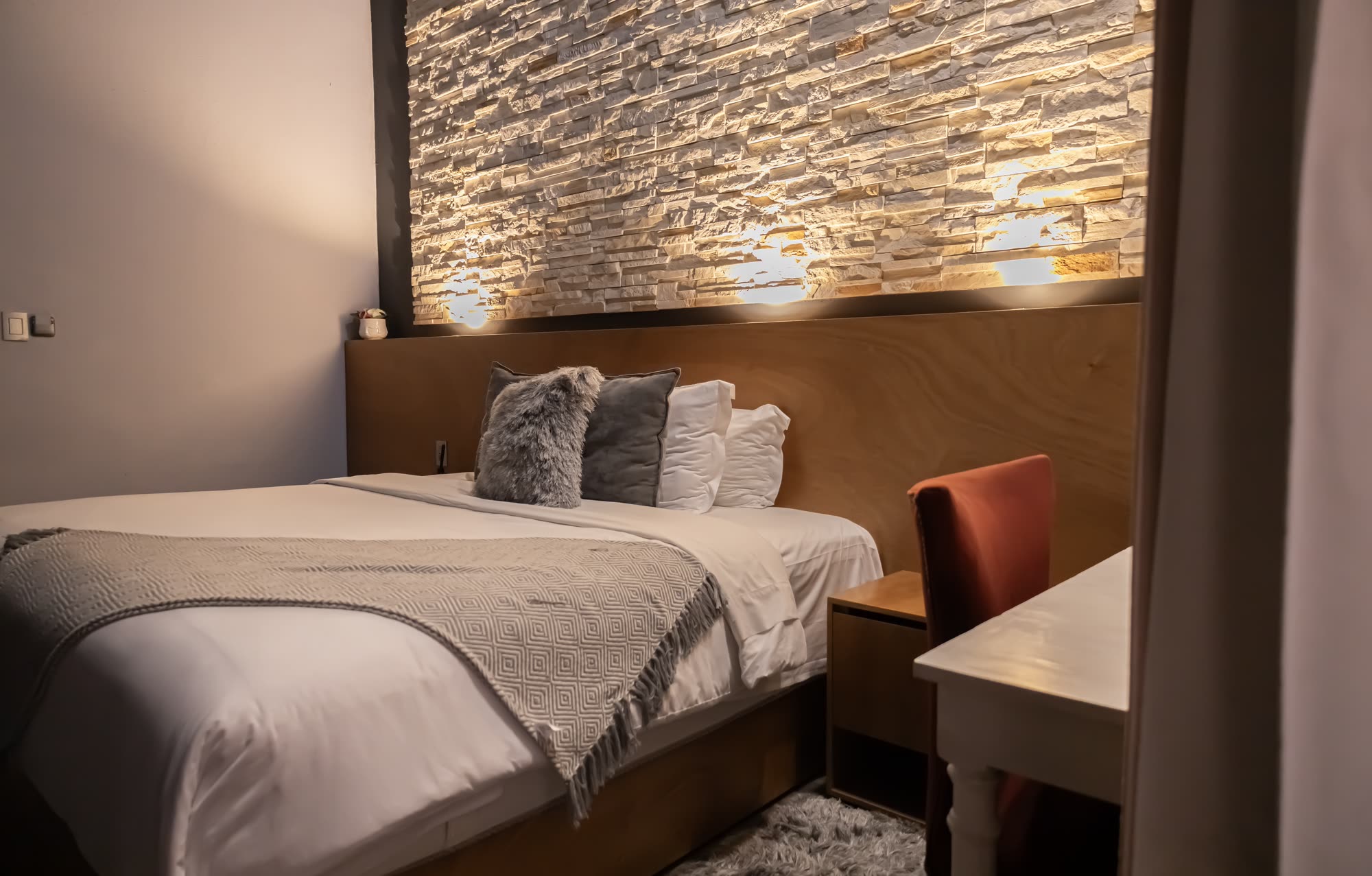 La cama de la habitación Deluxe 107 frente al muro de piedra iluminado