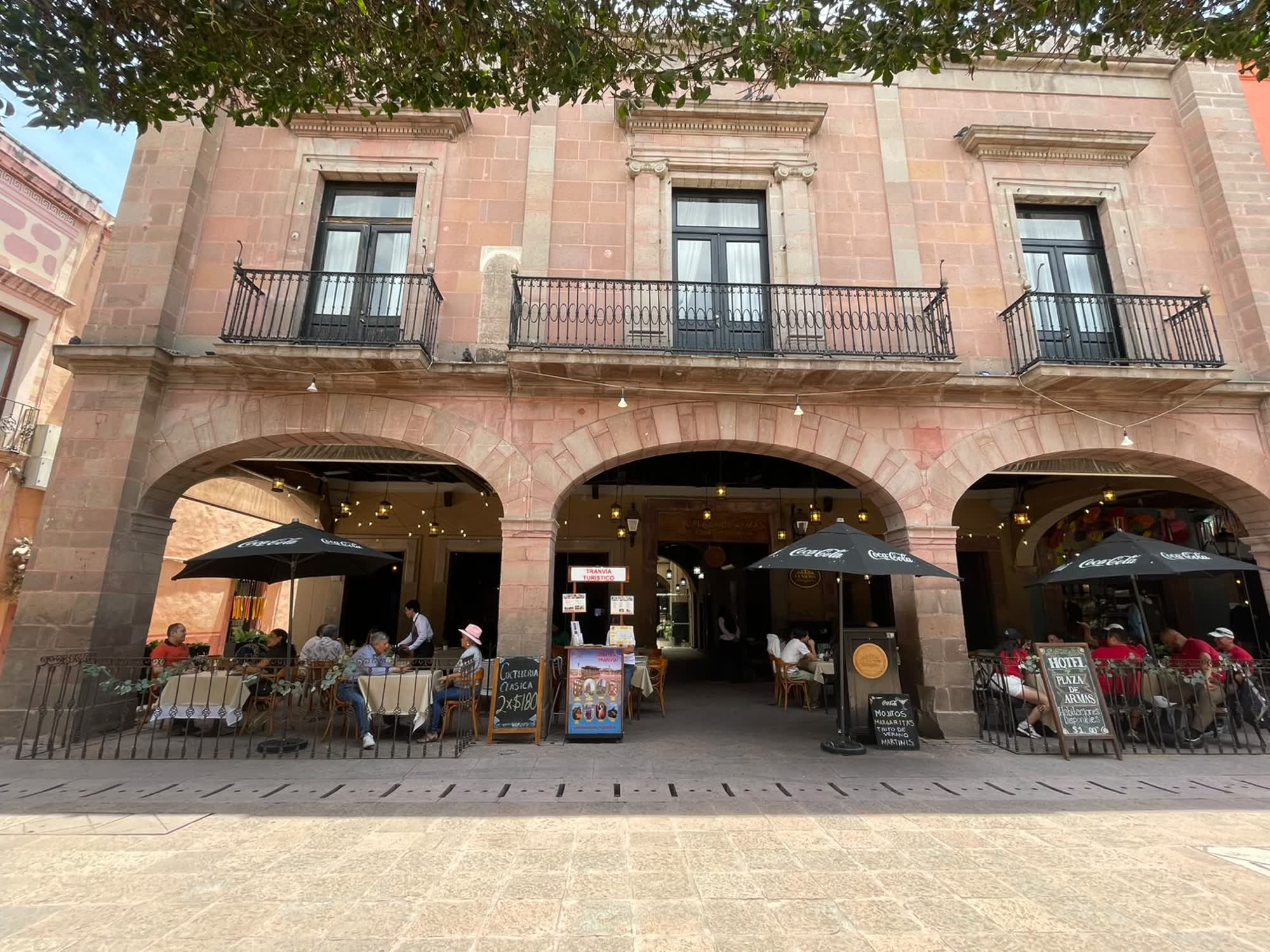 La fachada del hotel bajo los arcos de cantera del portal, con las mesas del restaurante en la banqueta
