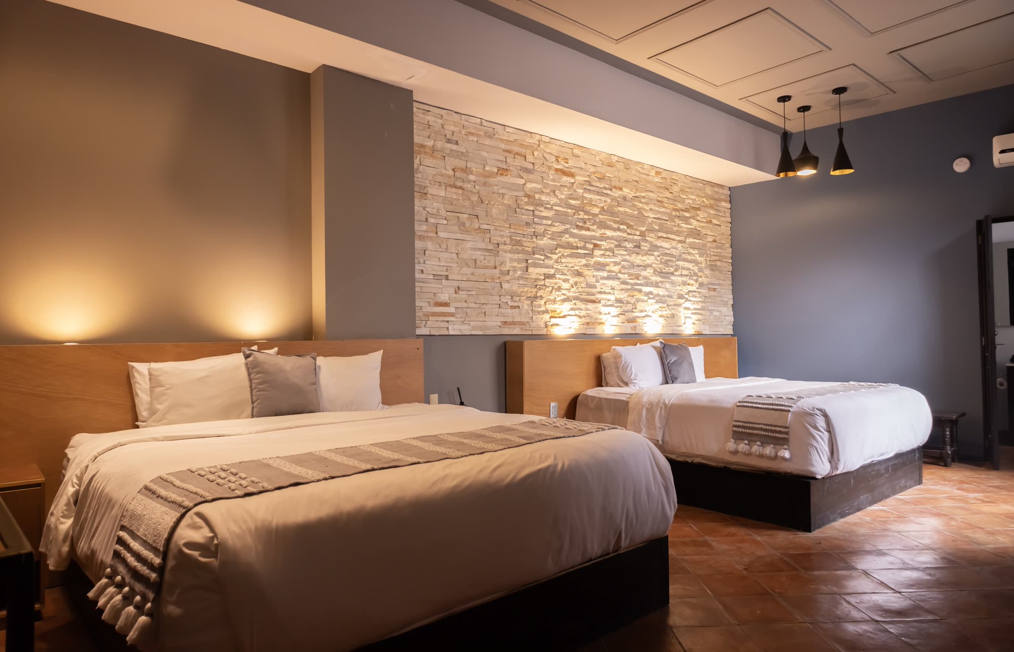 La Jr Suite Doble 203 con sus dos camas y muro de piedra iluminado
