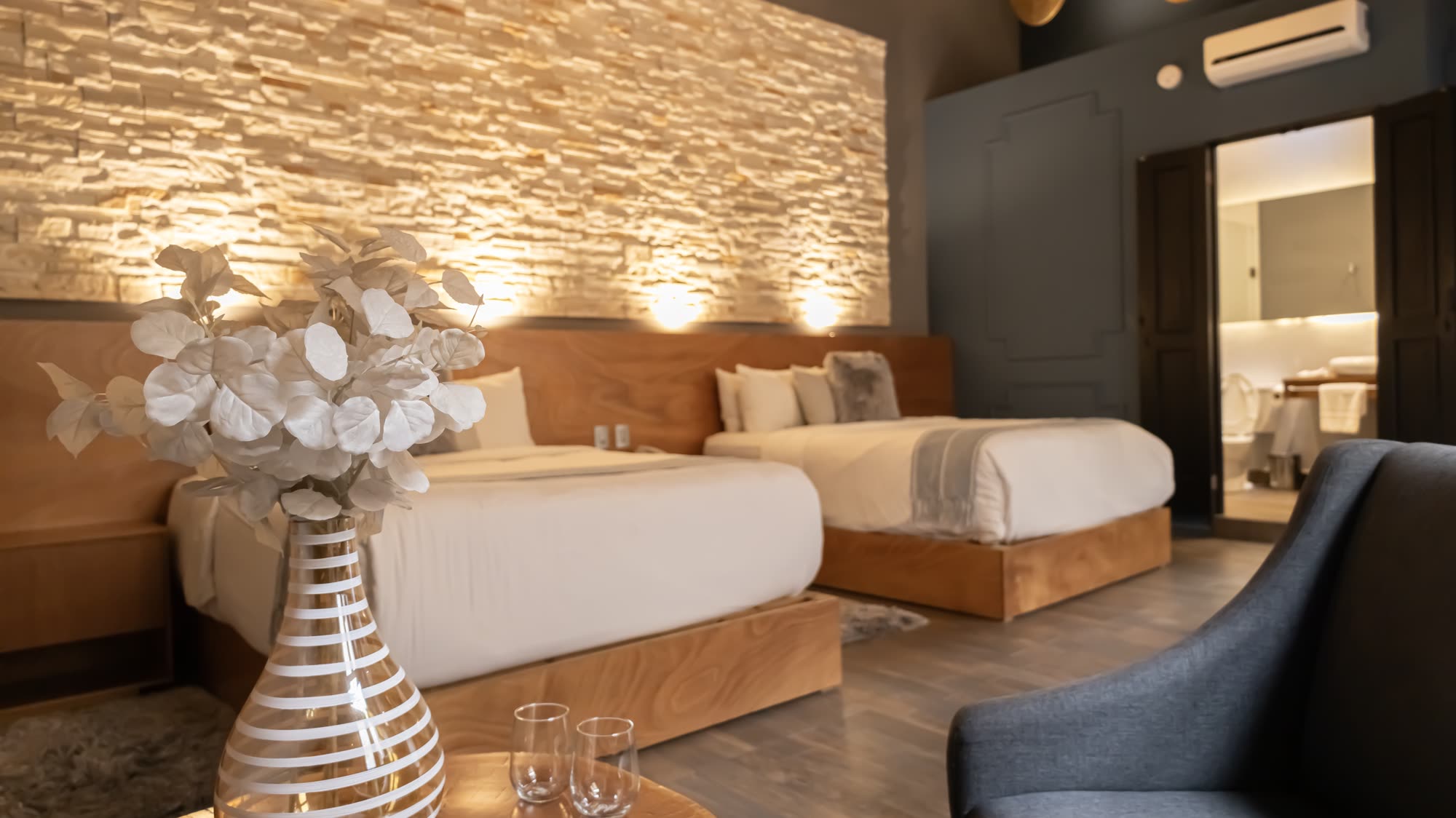La Jr Suite Doble 207 con sus dos camas y muro de piedra iluminado