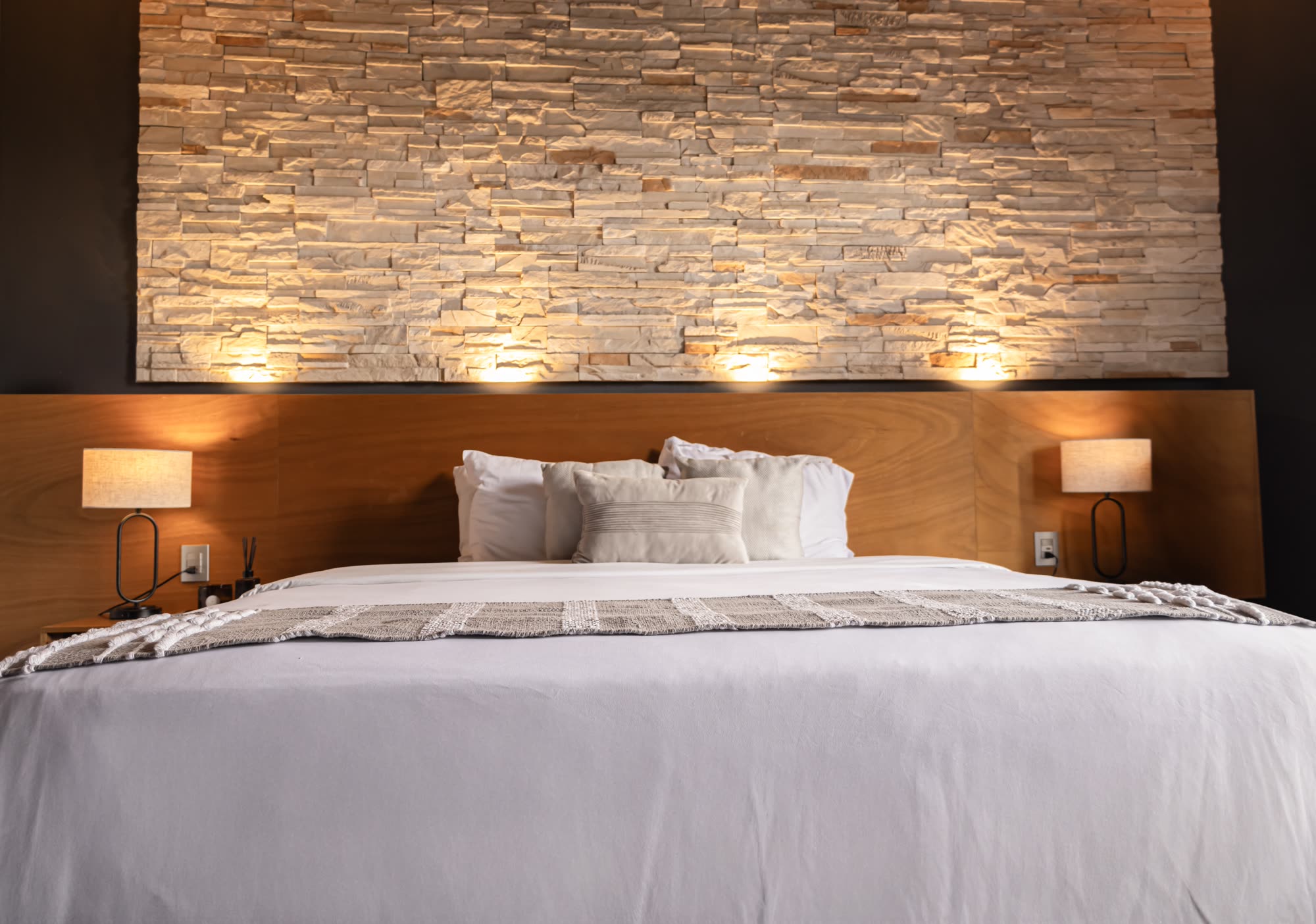 La cama de la Jr Suite Premium 211 frente al muro de piedra iluminado